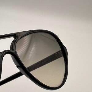 Puede incluir: Gafas de sol aviador negras con doble puente y lentes degradadas. Las gafas tienen una montura gruesa y un dise&ntilde;o cl&aacute;sico. Las lentes pasan de un tono m&aacute;s oscuro en la parte superior a un tono m&aacute;s claro en la parte inferior.