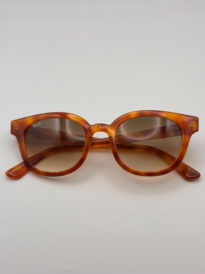 May include: Tortoiseshell sunglasses with a rounded frame and gradient lenses. The sunglasses have a classic design. The Ray-Ban logo is visible on the left lens. Suitable for everyday wear.