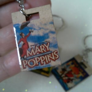 May include: A wooden keychain with a colorful image of Mary Poppins holding an umbrella and the text "Mary Poppins".
