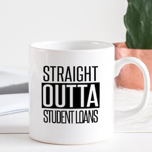 May include: White ceramic mug with the text "STRAIGHT OUTTA STUDENT LOANS" in black block letters. The mug is on a white surface with a book and a copper-colored pot with a plant in the background.