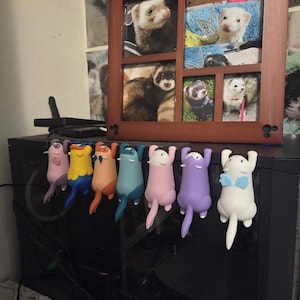 May include: A row of seven small, colorful animal-shaped figurines hanging from the edge of a black computer tower. The figurines are various colors including purple, yellow, orange, blue, pink, and white, each with a distinct tail and ears.