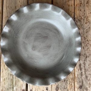 May include: A gray ceramic pie plate with a fluted edge. The plate is empty and has a slightly textured surface.