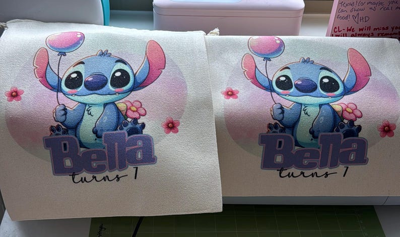 May include: Two white fabric bags with a blue Stitch character holding a pink balloon. The bags have the text "Bella turns 1" printed on them.