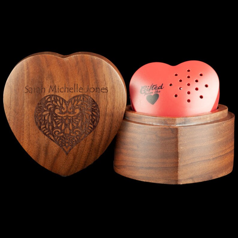 May include: A wooden heart-shaped box with a red heart-shaped music box inside. The box is engraved with the name "Sarah Michelle Jones" and the music box has the words "Gifted from the heart" on it.