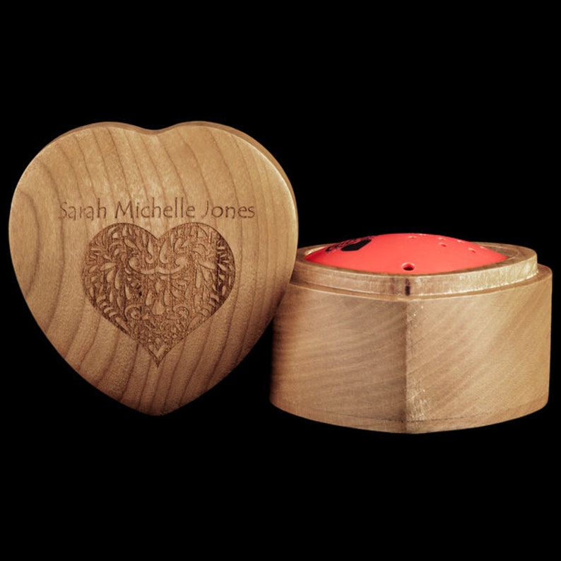 May include: A wooden heart-shaped box with the name "Sarah Michelle Jones" engraved on the front. The box is open and reveals a smaller wooden box with a red lid.