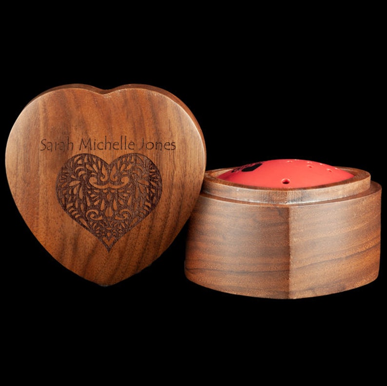 May include: A wooden heart-shaped box with an engraved design and the name "Sarah Michelle Jones" on the lid. The box is open and reveals a smaller, round wooden box with a red interior.