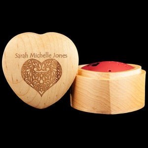 May include: A wooden heart-shaped box with the name "Sarah Michelle Jones" engraved on the front. The box has a carved heart design and is open to reveal a smaller wooden box with a red lid.