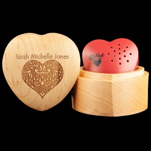 May include: A wooden heart-shaped box with a personalized inscription "Sarah Michelle Jones" and a carved heart design. The box is open and reveals a red heart-shaped music box with the inscription "Gifted from the heart".
