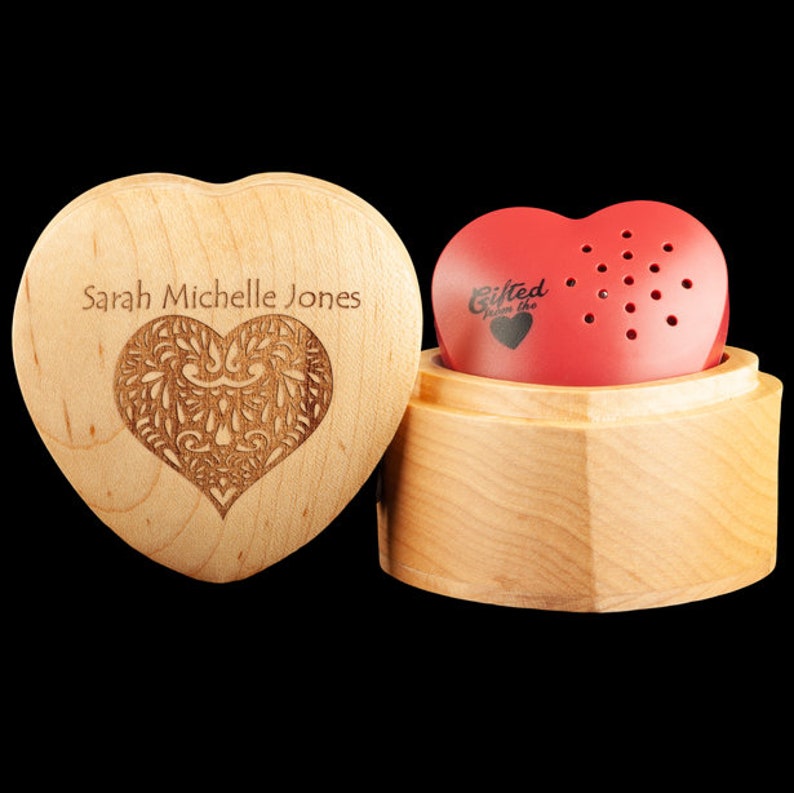 May include: A wooden heart-shaped box with a personalized inscription "Sarah Michelle Jones" and a carved heart design. The box is open and reveals a red heart-shaped music box with the inscription "Gifted from the heart".