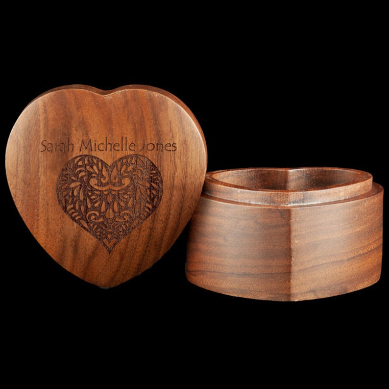 May include: A heart-shaped wooden box with a lid. The lid is engraved with the name "Sarah Michelle Jones" and a decorative heart design. The box is made of dark wood.