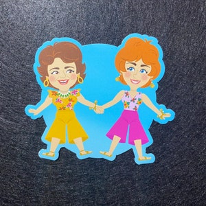 May include: Two cartoon women with brown and red hair wearing floral print tops and bright colored pants. They are holding hands and smiling.