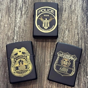 May include: Three black lighters with gold-colored police badges. The top lighter has a badge with the words "POLICE" and "NYPD" and the words "STRATEGIC RESPONSE GROUP". The middle lighter has a badge with the words "CITY OF NEW YORK POLICE" and "SERGEANT". The bottom lighter has a badge with the words "CITY OF NEW YORK POLICE".
