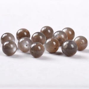 May include: A selection of spherical beads in shades of brown and grey. The beads have a shiny surface, reflecting light. These gemstone beads are suitable for jewellery making and craft projects.