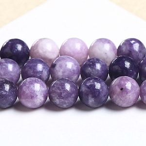 May include: A strand of purple and lavender gemstone beads. The beads are round and smooth, with a slight variation in colour.