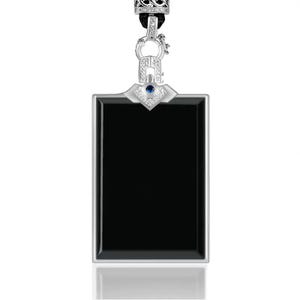 Puede incluir: Colgante rectangular negro con marco y detalles plateados. El colgante tiene una pequeña gema azul y está suspendido de un cordón negro. La parte superior tiene un cierre plateado decorativo.