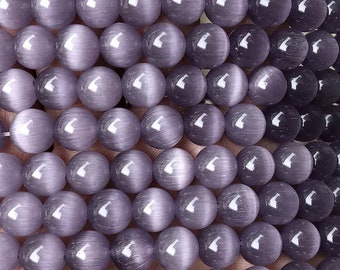 Pode incluir: Um fio de contas redondas de olho de gato roxo. As contas têm uma superfície lisa e polida e um brilho sutil.