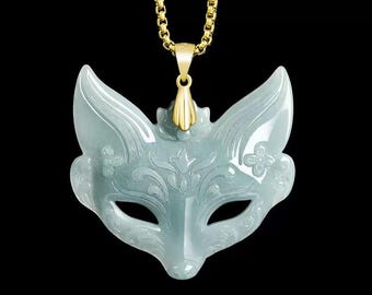 Puede incluir: Colgante de máscara de zorro de jade verde claro con cadena dorada. El colgante presenta intrincados diseños florales y de remolinos y está suspendido de una fianza dorada. La máscara tiene aberturas para los ojos y orejas puntiagudas.
