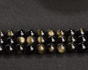 May include: A strand of black beads with gold flecks. The beads are round and smooth, and they are arranged in a row.