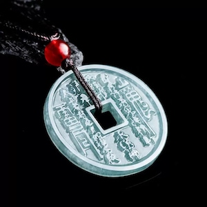 May include: A light green jade pendant necklace. The pendant is a circular coin shape with intricate carvings and a square hole in the center. The necklace has a black cord and a red bead.
