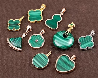 May include: A collection of malachite pendants in various shapes, including clover, gourd, and heart designs. The pendants have gold or silver-colored settings and showcase the stone's distinctive green and striped patterns. The pendants are displayed on a brown surface.
