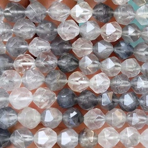 May include: A strand of faceted, clear quartz beads with a smoky grey hue. The beads are faceted and have a slightly irregular shape.