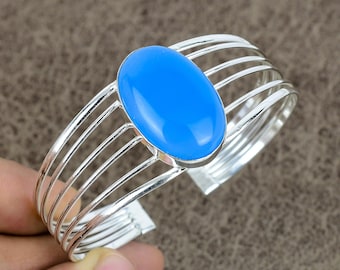 May include: A silver cuff bracelet featuring a large, oval, bright blue gemstone. The bracelet has a multi-band design with parallel silver bars. The gemstone is the focal point, set in a silver bezel.
