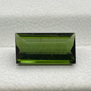 May include: A dark green rectangular gemstone with a faceted cut.