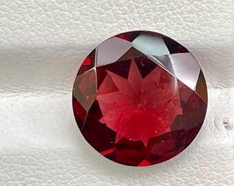 May include: A round, faceted, red gemstone with a star-shaped pattern inside. The gemstone is set on a white background.