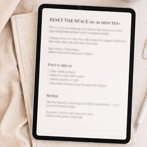 May include: A black tablet displaying the text "RESET THE SPACE (15-30 MINUTES)" on a white background. The tablet rests on a beige cloth, with a cup of coffee and a pen nearby. The image has a minimalist aesthetic.