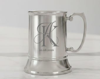 May include: A silver-colored beer stein with a handle, featuring an engraved monogram and the date 10.08.2026. The stein has a classic shape with a wide base and a flared top, perfect for personalized gifts.