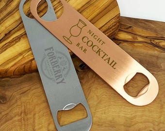 May include: Two metal bottle openers. One is silver with the text "FORBERRY CRAFT BEER". The other is copper-colored with the text "NIGHT COCKTAIL BAR" and a cocktail glass graphic. Both have a hole for hanging.