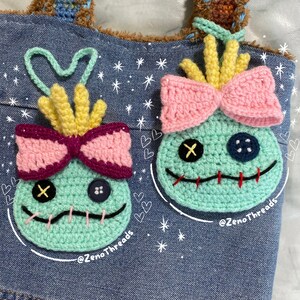 Pu&ograve; includere: Due personaggi Stitch all'uncinetto di Lilo & Stitch, con fiocchi rosa e capelli gialli, sono attaccati a una borsa di jeans. La borsa ha uno sfondo bianco con stelle e cuori.