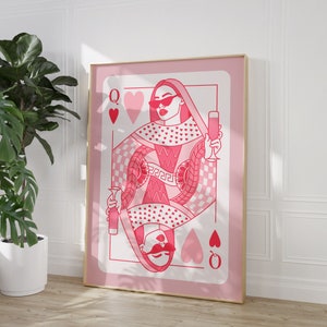 May include: A pink playing card with a queen of hearts design. The queen is wearing sunglasses and holding a glass of champagne. The card has a pink and white checkered pattern and is surrounded by hearts.