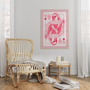 May include: A pink and white illustration of the Queen of Hearts playing card. The Queen is wearing sunglasses and holding a glass of wine. The card is framed and hanging on a wall.