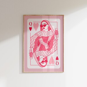 May include: A pink playing card with a queen of hearts design. The queen is wearing sunglasses and holding a glass of champagne. The card has a pink background with a checkered pattern and hearts.