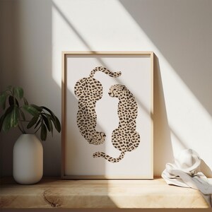 May include: A framed print featuring a minimalist illustration of two cheetahs in a beige and brown color scheme, facing each other in a circular formation.