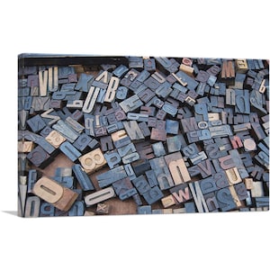 May include: A close-up of a collection of vintage wooden letterpress printing blocks. The blocks are arranged in a random pattern and are made of different types of wood. The letters are all in uppercase and are painted in shades of blue, brown, and gray.