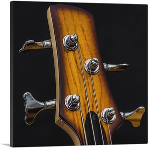 May include: Close-up of the headstock of a bass guitar with a natural wood finish. The tuning pegs are silver and the strings are black.