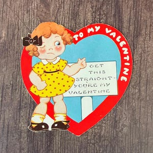 May include: A vintage Valentine's Day card featuring a cartoon girl with red hair and a yellow polka dot dress. The girl is holding a sign that says "Get this straight - You're my Valentine". The card is shaped like a heart with a red border and a blue center.