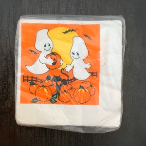 May include: A package of white paper napkins with a Halloween design. The design features two ghosts, a black cat, and pumpkins on an orange background.