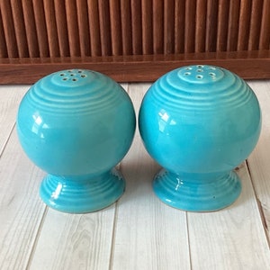 May include: Two blue ceramic salt and pepper shakers with a ribbed design. The shakers have a round body and a small base.