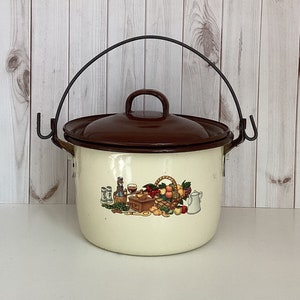 May include: White enamel pot with a brown lid and a black metal handle. The pot has a colorful illustration of a basket of fruit, wine bottles, and kitchen utensils.