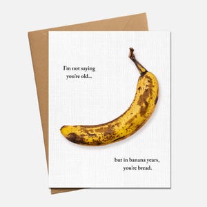 May include: Greeting card with a ripe banana illustration. The banana is yellow with brown spots, and the card has the text: "I'm not saying you're old... but in banana years, you're bread."