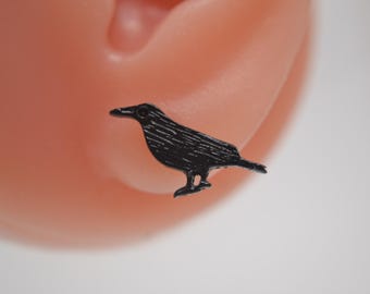 May include: A black crow earring, a small, detailed silhouette of a crow with a slightly open beak.