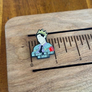 Pode incluir: Um alfinete de esmalte colorido com uma figura de desenho animado usando uma coroa e uma jaqueta estampada. O alfinete tem o texto "NO DOUBT, NO DOUBT, NO DOUBT!" e &eacute; colocado em uma r&eacute;gua de madeira. A r&eacute;gua tem aproximadamente 7,6 cm de comprimento.
