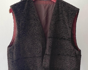 May include: A brown faux fur vest with a V-neck and two pockets. The vest is hanging on a black metal hanger.