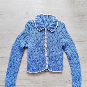 Könnte beinhalten: Ein blauer Strickcardigan mit einem weißen Häkelkragen und Knöpfen.