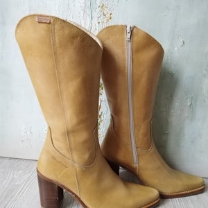 K&ouml;nnte beinhalten: Ein Paar kniehohe Stiefel aus hellbraunem Leder mit Blockabsatz und seitlichem Rei&szlig;verschluss. Die Stiefel haben eine spitze Zehenpartie und eine gen&auml;hte Sohle. Der Absatz ist ca. 7.6 cm hoch.