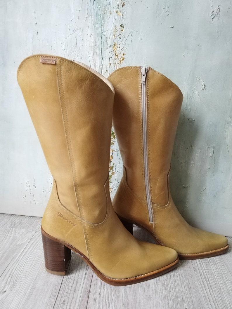 K&ouml;nnte beinhalten: Ein Paar kniehohe Stiefel aus hellbraunem Leder mit Blockabsatz und seitlichem Rei&szlig;verschluss. Die Stiefel haben eine spitze Zehenpartie und eine gen&auml;hte Sohle. Der Absatz ist ca. 7.6 cm hoch.