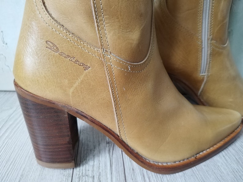 K&ouml;nnte beinhalten: Hellbraune Leder-Ankle Boots mit spitzer Zehenpartie und Blockabsatz. Die Stiefel haben einen Rei&szlig;verschluss an der Seite und das Wort "Destroy" ist eingepr&auml;gt. Der Absatz ist ca. 7,6 cm hoch.